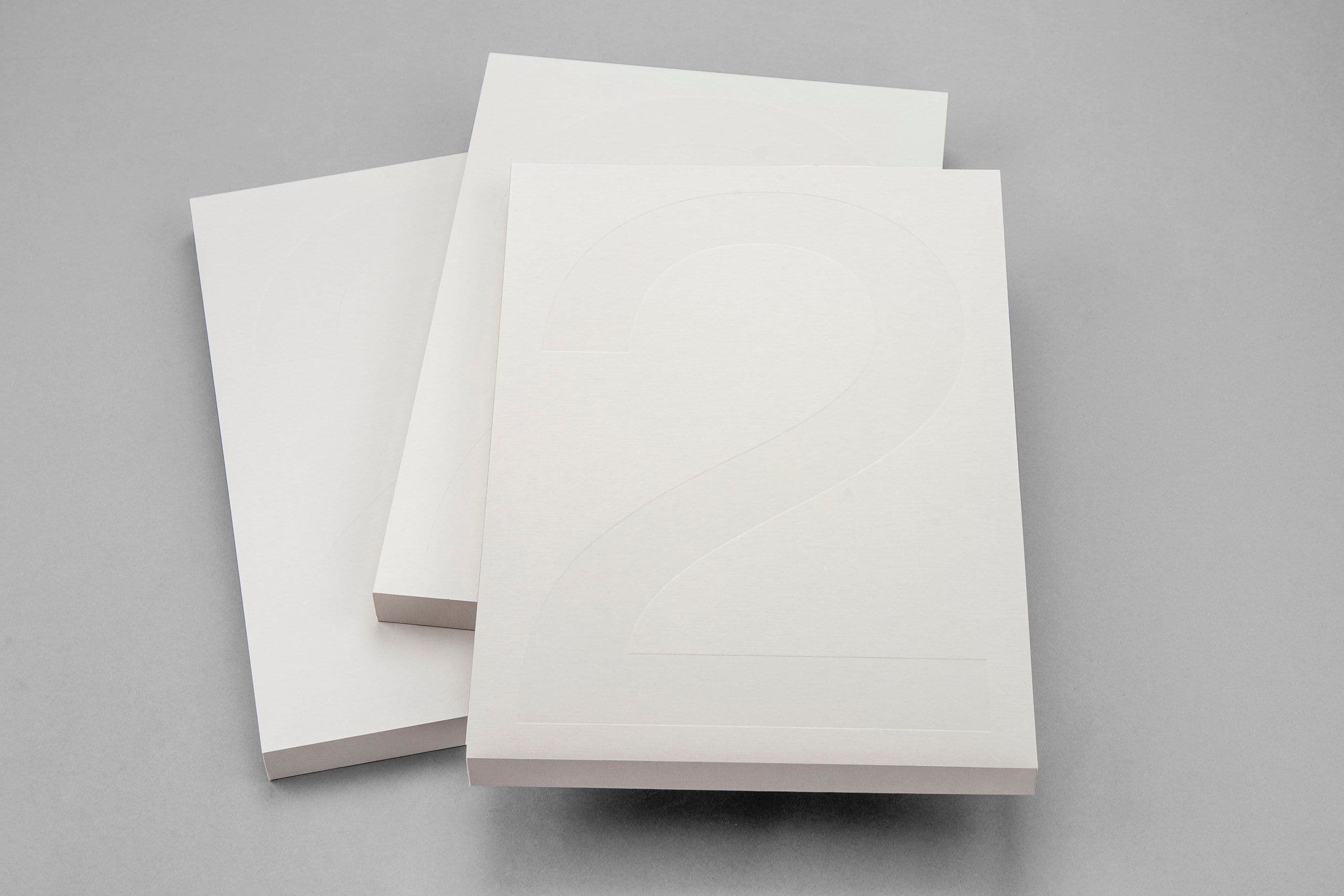 Minimalist white hardcover books with subtle embossed numbering, showcasing premium print finishing and refined production craftsmanship. The image highlights precision embossing, high-quality paper stock, and clean case binding—ideal for luxury brand books, limited-edition publications, corporate reports, and custom presentation materials. A strong example of multi-solution print and packaging expertise, combining advanced print technology, specialty finishes, and premium material selection for high-end brand communication.