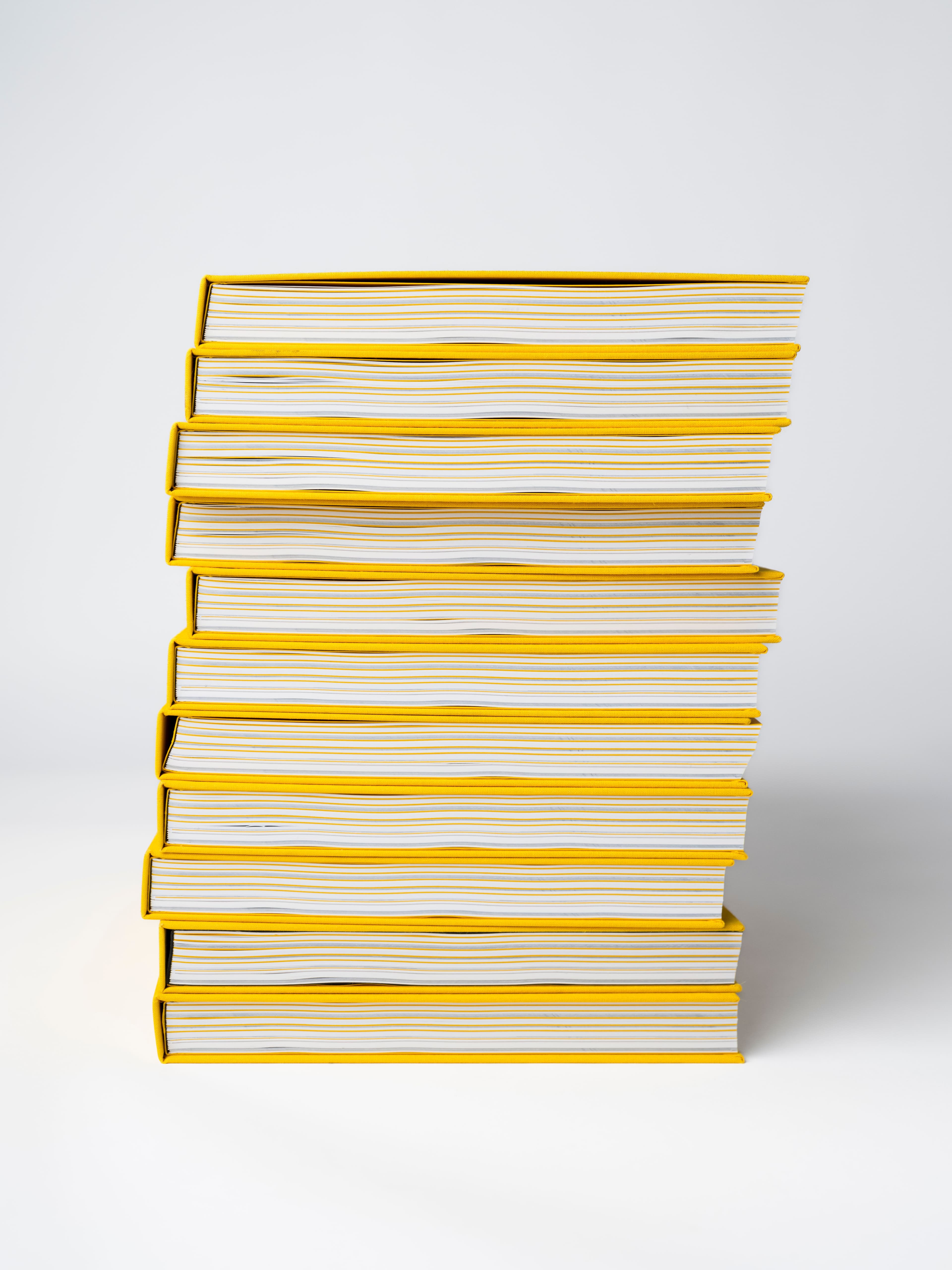 Stack of premium hardcover books with vibrant yellow cloth binding, showcasing high-quality book printing and professional binding solutions. The image highlights precision craftsmanship, durable case binding, and clean page finishing—ideal for brand books, corporate reports, luxury catalogs, and custom publications. A strong example of multi-solution print production combining design, materials, and expert finishing for premium brand communication.